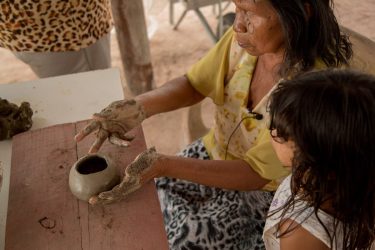 Português: A mestra ensina sua neta a fazer cerâmica. Karajá: Bdèkèry taritxokorè rikèrynanyrèri suu widkỹ.